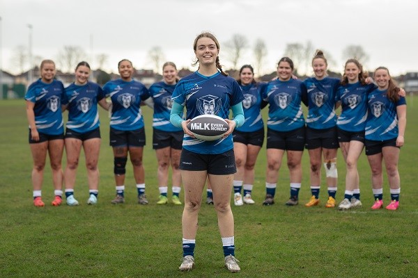 A girl holding a rugby ball with the rest of the team standing behind her.
